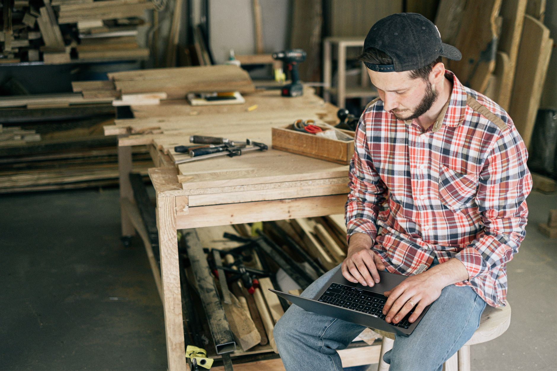 A small business owner at a workbench checking their phone and laptop